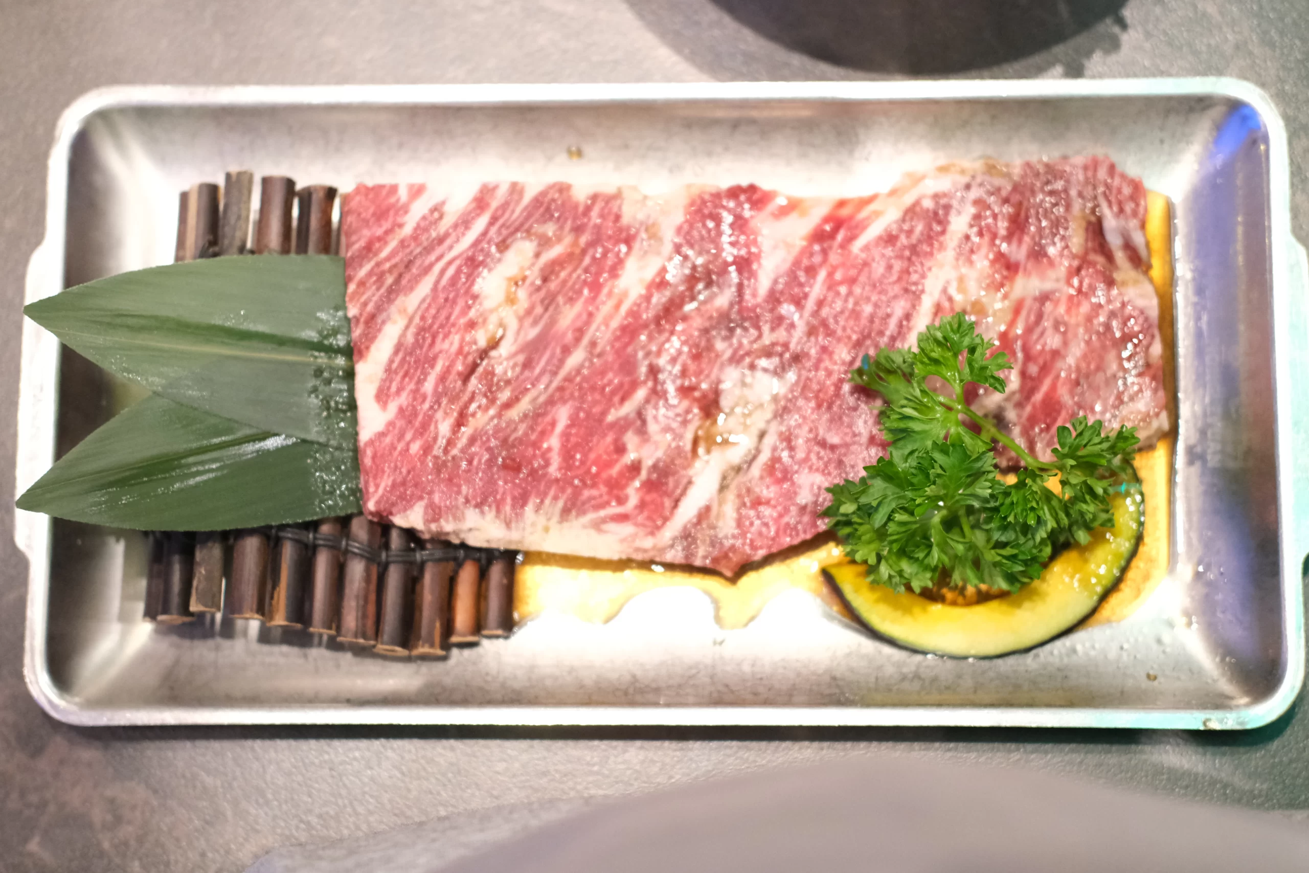 A single piece of glazed meat sizzling on a hot grill with visible flames beneath the grates.