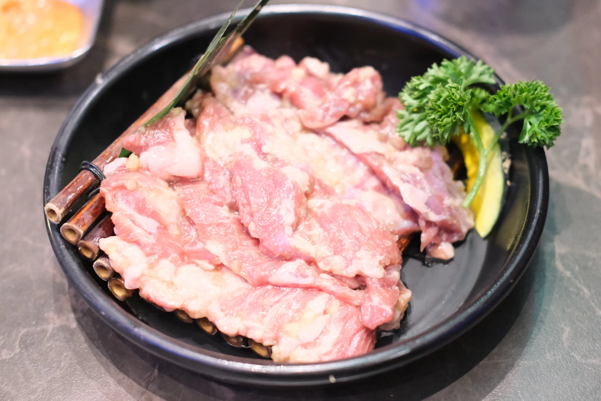 Grilled meat with distinct char marks being basted with sauce on a barbecue grill using a silicone brush.